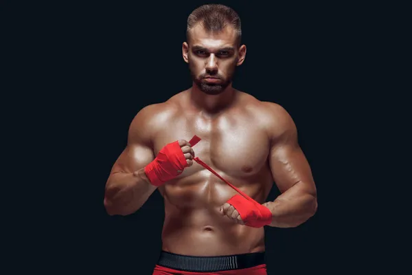 Muscular young fighter is applying bondage tape on hands getting ready to fight isolated on black background — Stock Photo, Image