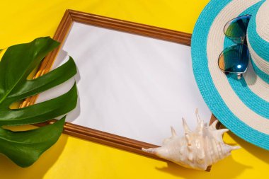 Çizgili mavi şapka, güneş gözlüğü, canavar yaprağı, deniz kabuğu ve sarı arka planda tatil fotoğrafları için çerçeve. Plaj tatili kavramı, deniz turu, sıcak güneşli yaz. Kopyala-yapıştır