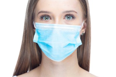 Coronavirus hastalığından dolayı stres altında maske takan genç bir kadının yakın plan portresi beyaz arka planda izole edilmiş kameraya bakıyor. Grip salgını, toz alerjisi, virüse karşı koruma