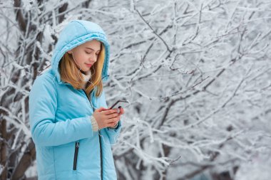 Şirin, gülümseyen genç bir kadının videoları akıllı telefondan izlediği ya da kar parkında yürürken kulaklıkla müzik dinlediği bir fotoğraf.