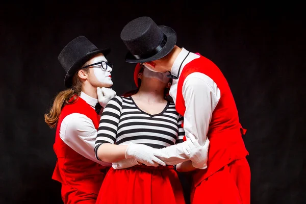 Portrait of three mime artists, isolated on black background. A man joins the heads of a man and a woman in a kiss. Symbol of procurement, Cupid, matchmaker — Stock Photo, Image