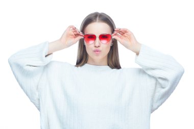 Göz kamaştırıcı bir kadının stüdyo portresi. Kırmızı güneş gözlüğü takıyor. İki eli yüzü de beyaz arka planda.