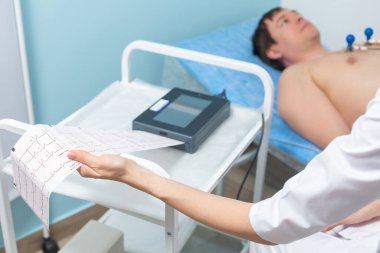 Klinikteki doktor randevusu sırasında kardiyogramın çıktısını alan bir elektrokardiyografın yakın plan fotoğrafı.