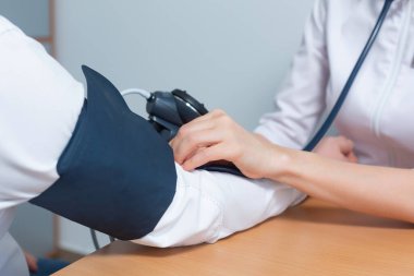Kadın bir doktor, hipertansiyonu ve kalp krizini önlemek için tıbbi muayene sırasında erkek bir hastanın kan basıncını ölçer.