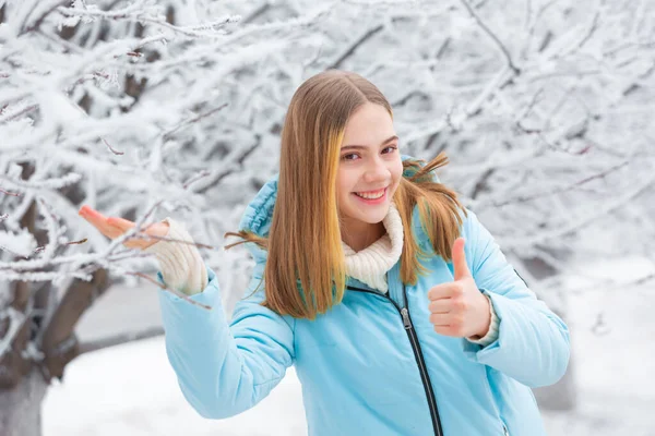 Közel kép csinos fiatal nő áll mosolyogva a havas téli erdőben mutató hüvelykujj fel gesztus — Stock Fotó