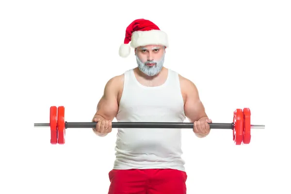Święta. Silny umięśniony Święty Mikołaj z szarą brodą w świątecznym kapeluszu i czerwonych spodenkach podnosi ciężką sztangę na siłowni wykonując trening na białym tle — Zdjęcie stockowe