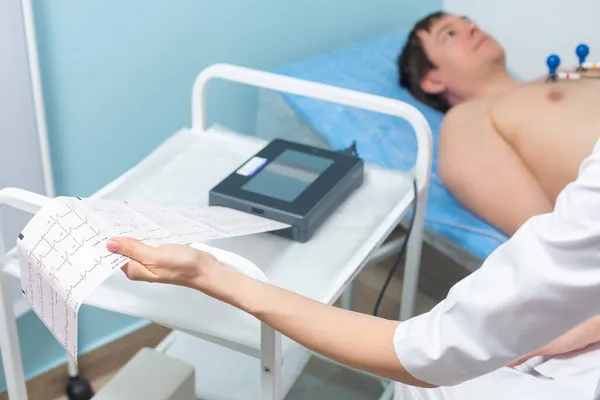Nahaufnahme eines Elektrokardiographen, der die Ergebnisse eines Kardiogramms während eines Arzttermins in der Klinik ausdruckt — Stockfoto