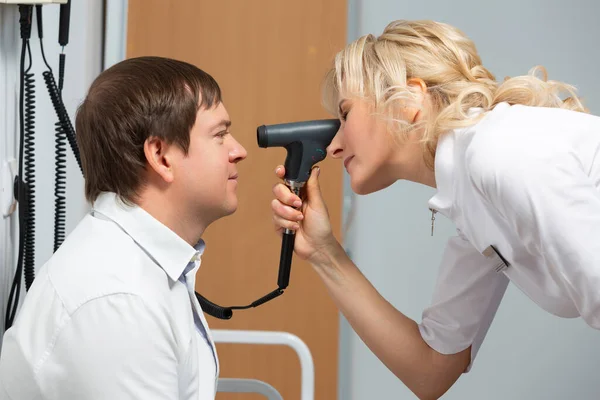 Um oftalmologista realiza um exame médico de um paciente do sexo masculino usando um oftalmoscópio. Oculista usando dispositivo especial tentando melhorar a visão de um homem para a saúde dos olhos — Fotografia de Stock