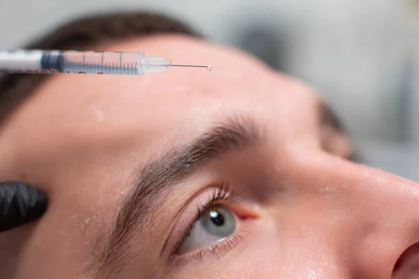 Close-up de uma gota de uma droga caindo de uma agulha de seringa na testa de um paciente masculino de um escritório de cosmetologia. Procedimento de rejuvenescimento, injeções de botox contra rugas faciais — Fotografia de Stock