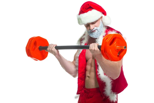 Navidad. Santa Claus musculoso fuerte con la barba gris que usa el sombrero de Navidad y los pantalones cortos rojos está levantando una barra pesada en un gimnasio que realiza un entrenamiento aislado en fondo blanco. — Foto de Stock