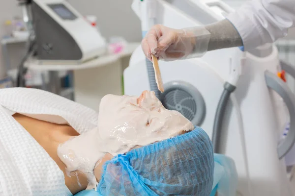 El cosmetólogo aplicando una máscara de alginato a la cara de una joven mujer acostada en el salón de belleza para el procedimiento de limpieza e hidratación de la piel, eliminando la hinchazón y el efecto lifting — Foto de Stock