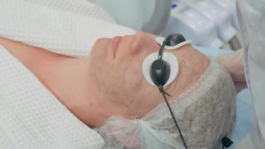 Kozmetik prosedürü. Güzellik salonunda karbon soyma işlemi sırasında koruyucu gözlük takan genç bir kızın yüzü.