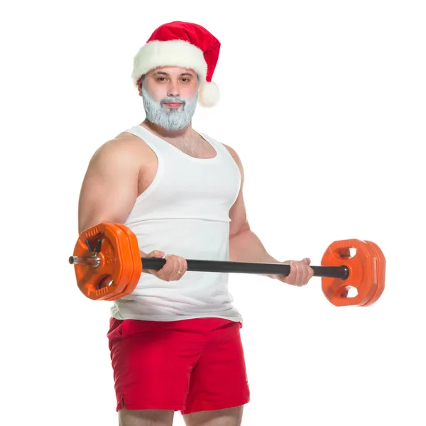 Navidad. Santa Claus musculoso fuerte con la barba gris que usa el sombrero de Navidad y los pantalones cortos rojos está levantando una barra pesada en un gimnasio que realiza un entrenamiento aislado en fondo blanco — Foto de Stock