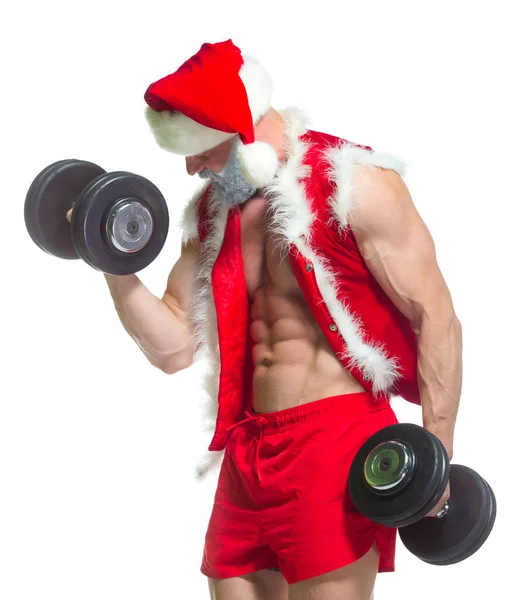 Navidad. Santa Claus musculoso fuerte con barba gris con sombrero de Navidad y pantalones cortos rojos está levantando unas pesadas mancuernas en un gimnasio realizando un entrenamiento aislado sobre fondo blanco. — Foto de Stock