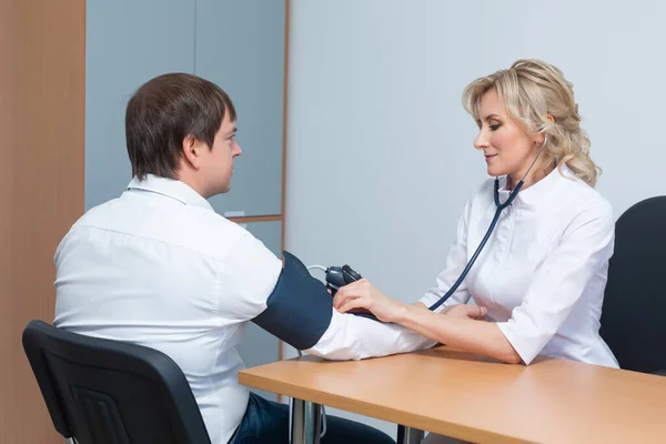 Uma médica do sexo feminino mede a pressão arterial de um paciente do sexo masculino durante um exame médico para evitar hipertensão e ataque cardíaco — Fotografia de Stock