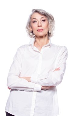 Yetişkin, kendine güvenen, beyaz saçlı, kollarını kavuşturmuş gülümseyen ve beyaz arka planda izole edilmiş kameraya bakan bir kadının resmi.