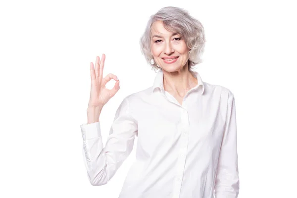 Retrato de una mujer atractiva madura con camisa elegante de pie sobre un fondo blanco aislado sonriendo con la cara feliz haciendo signo de bien —  Fotos de Stock