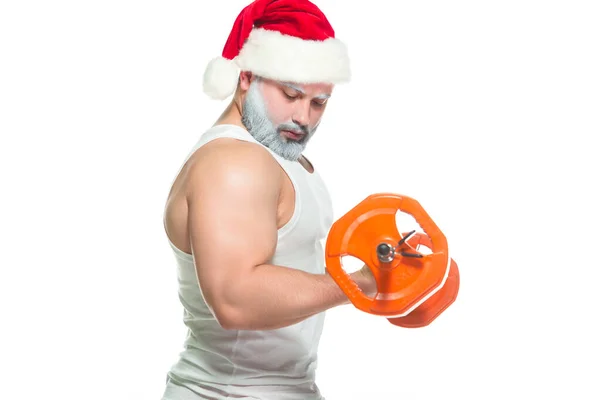Navidad. Santa Claus musculoso fuerte con la barba gris que usa el sombrero de Navidad y los pantalones cortos rojos está levantando una barra pesada en un gimnasio que realiza un entrenamiento aislado en fondo blanco — Foto de Stock