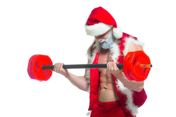 Święta. Silny umięśniony Święty Mikołaj z szarą brodą w świątecznym kapeluszu i czerwonych spodenkach podnosi ciężką sztangę na siłowni wykonując trening na białym tle. — Zdjęcie stockowe