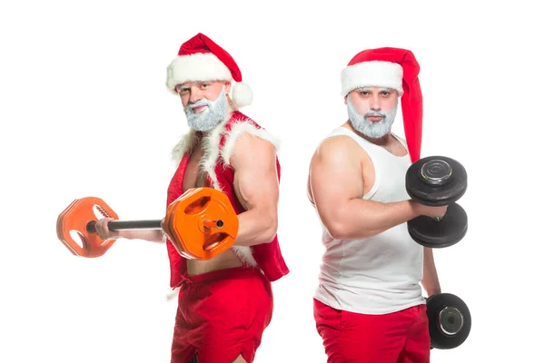 Święta. Portret dwóch silnych muskularnych brodatych sportowców w kostiumach Świętego Mikołaja, trening przez podnoszenie sztangi wyizolowanych na białym tle — Zdjęcie stockowe