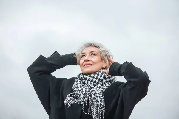 Porträtt av en fri, självständig och glad mogen kvinna i varma kläder mot en grå hösthimmel — Stockfoto