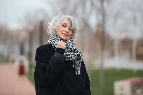 Retrato de una hermosa mujer madura caminando en el parque de otoño en un abrigo y una bufanda de moda caliente —  Fotos de Stock