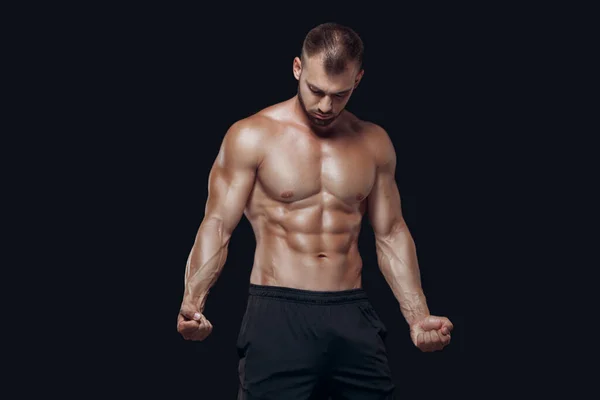 若い筋肉とフィット若いボディビルダーフィットネス男性モデルポーズと黒の背景に隔離された彼の筋肉を実証 — ストック写真
