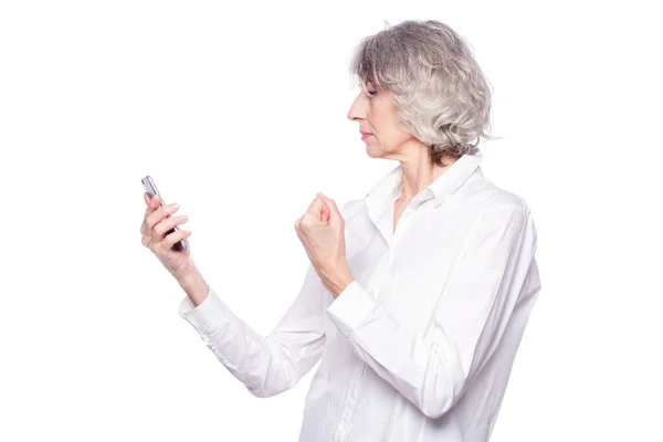 Eine sympathische Seniorin sieht sehr wütend und genervt aus, während sie mit ihrem Handy telefoniert. Schüttelt seine Faust gegen Telefonbetrüger isoliert auf weißem Hintergrund — Stockfoto