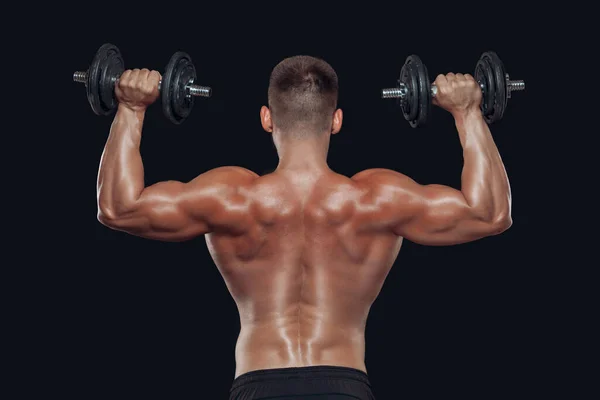 Vista posterior cercana del cuerpo muscular y manos fuertes levantando pesadas mancuernas aisladas sobre fondo negro — Foto de Stock