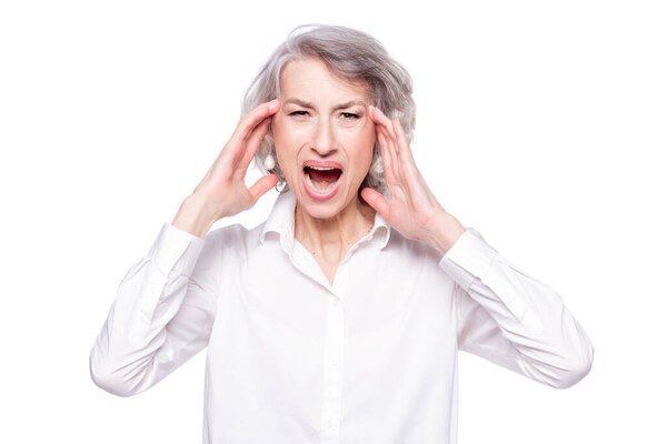 Studio shot of distressed irritated senior woman losing temper screaming out loud from pain and holding hands on head troubled and concerned being pissed and fed up, isolated on white background