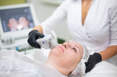 Kozmetoloji ofisinde bir kadın SMAS kaldırma prosedürü uygulanıyor. Cerrahi olmayan ultrason yüz gerdirme, gençleştirme, nemlendirme, kırışıklıklardan, cilt renginden ve esneklikten kurtulma.