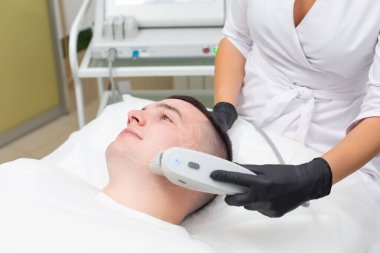 Kozmetoloji ofisinde çalışan bir adam SMAS kaldırma prosedürü uygulanıyor. Cerrahi olmayan ultrason yüz gerdirme, gençleştirme, nemlendirme, kırışıklıklardan, cilt renginden ve esneklikten kurtulma.