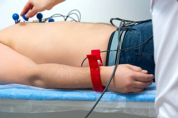 Una foto del cuerpo de un hombre acostado con un torso desnudo con sensores en el pecho y los brazos durante un procedimiento de electrocardiografía en una cita con un cardiólogo en la clínica — Foto de Stock
