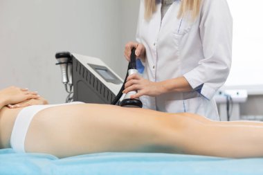 İnce bir kadın, ultrason etkisiyle yağ hücrelerini ayırmak için güzellik salonunda sıkı kalçalarına anti-selülit ve anti-yağ terapisi uygular.