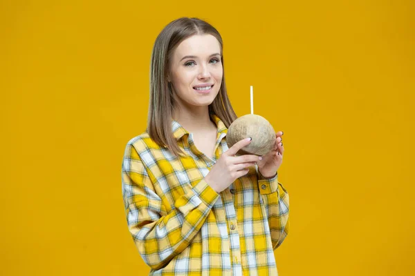 Portrait d'une belle jeune femme souriante tenant dans les deux mains de la noix de coco avec une paille isolée sur fond jaune. Concept de mode de vie sain, bonne nutrition, alimentation, végétalien, végétarien — Photo
