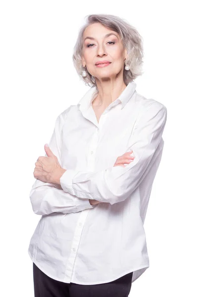 Glückliche trendige Seniorin mit einem schönen Lächeln, die ein modisches Hemd trägt und mit verschränkten Armen in die Kamera schaut, isoliert auf weißem Hintergrund — Stockfoto