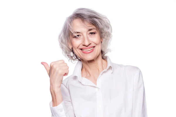 Close up portrait of a happy smiling mature woman in her sixties with trendy grey hair making thumbs up hand sign expressing approval isolated on white background — Stock Photo, Image