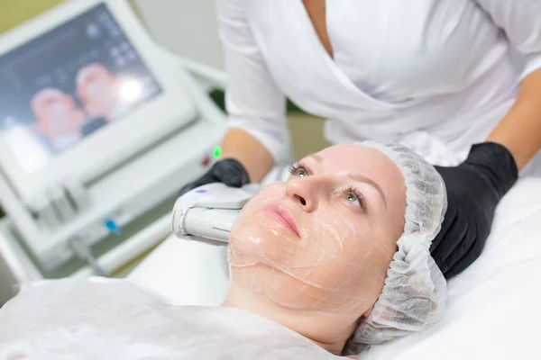 Uma mulher em um escritório de cosmetologia recebe um procedimento de elevação SMAS. Ultra-som não cirúrgico facelift, rejuvenescimento, hidratação, livrar-se de rugas, tom de pele e elasticidade — Fotografia de Stock