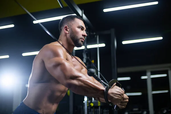 Side view portrait of a bodybuilder working on his chest muscles with cable crossover in a gym — Stock Photo, Image