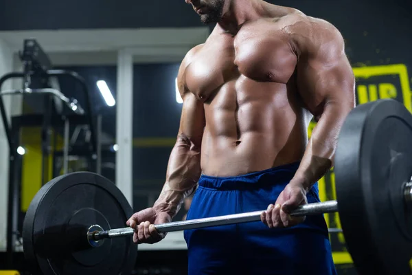 Acercamiento de un torso muscular desnudo y brazos fuertes levantando una pesada barra mientras entrena en un gimnasio — Foto de Stock