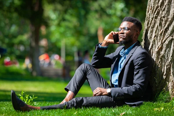 Afro-Amerikan bir adamın parktaki bir ağacın yanında cep telefonuyla konuşması gibi şık bir iş. — Stok fotoğraf