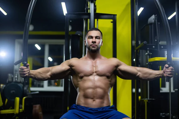 Atractivo culturista está haciendo ejercicio en un gimnasio entrenar sus músculos del pecho utilizando equipos deportivos —  Fotos de Stock