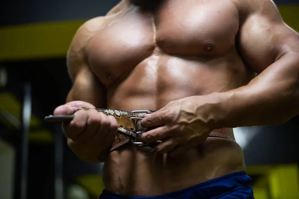 Acercamiento de un cuerpo desnudo hombre tonificado poniéndose un cinturón de levantamiento de pesas antes de entrenar en el gimnasio — Foto de Stock