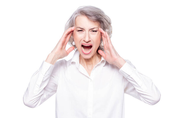 Studio shot of distressed irritated senior woman losing temper screaming out loud from pain and holding hands on head troubled and concerned being pissed and fed up, isolated on white background
