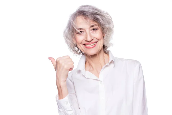 Retrato de cerca de una feliz mujer madura sonriente en sus sesenta años con el pelo gris de moda haciendo pulgares hacia arriba signo de la mano expresando su aprobación aislada sobre fondo blanco —  Fotos de Stock