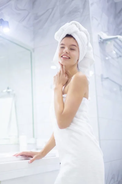 Retrato da jovem mulher sorridente feliz em pé no banho em toalhas brancas enroladas em torno de sua cabeça e corpo após o banho da manhã — Fotografia de Stock