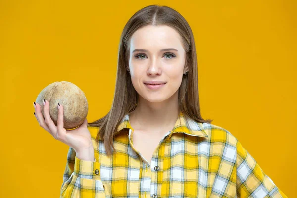 Portrait d'une jeune femme heureuse debout avec une noix de coco dans une main levée isolée sur fond jaune. Concept de mode de vie sain, bonne nutrition, alimentation, végétalien, végétarien — Photo
