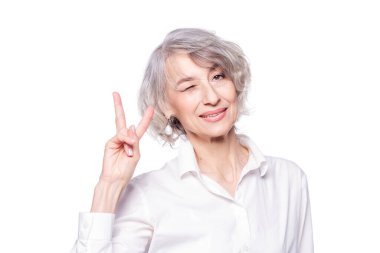 Gri saçlı, zarif tişörtlü yaşlı bir kadının portresi. İzole edilmiş beyaz arka planda duruyor. Gülümsüyor ve kameraya gülümsüyor.