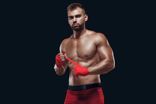 Muscular jovem lutador está aplicando fita de escravidão em mãos se preparando para lutar isolado no fundo preto — Fotografia de Stock