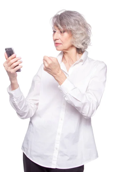 Eine sympathische Seniorin sieht sehr wütend und genervt aus, während sie mit ihrem Handy telefoniert. Schüttelt seine Faust gegen Telefonbetrüger isoliert auf weißem Hintergrund — Stockfoto